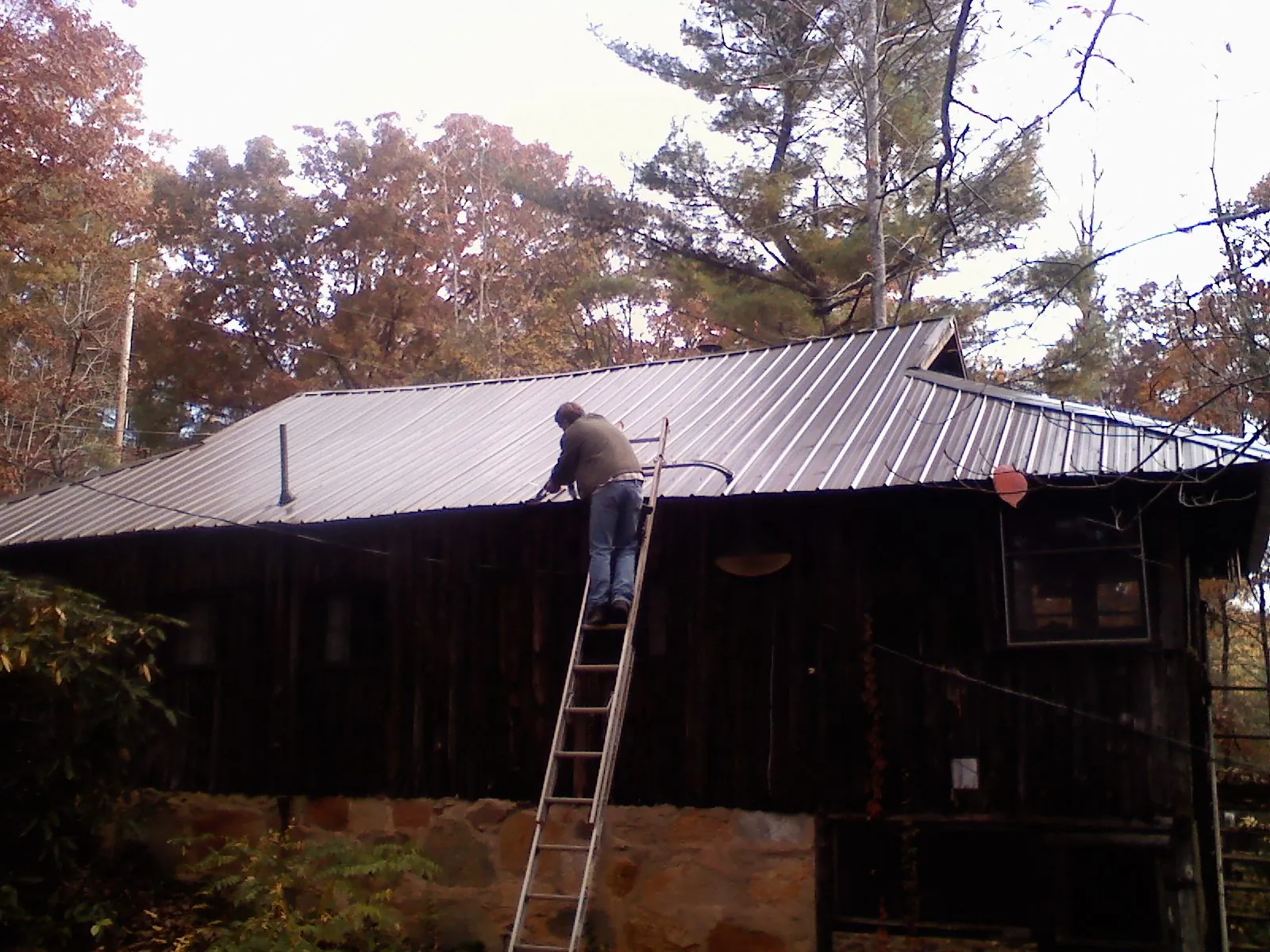 Roofer on a ladder working along the edge of a cabin metal roof in Verona